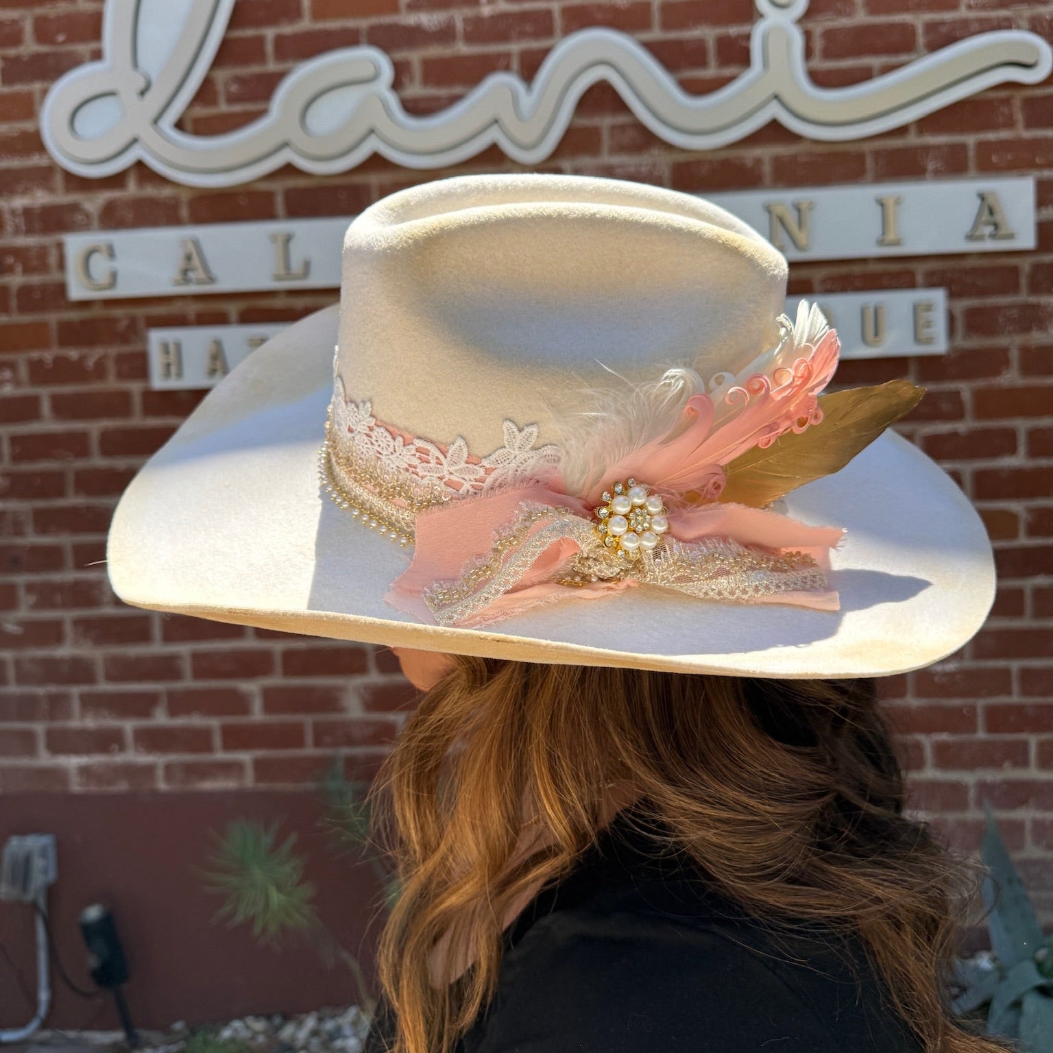 Person wearing a custom decorative hat with a brick wall and sign in the background