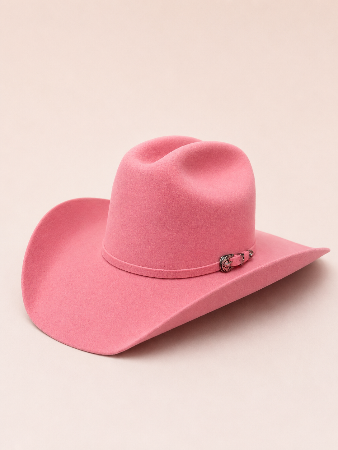 A pink felt cowboy hat with a small silver-toned decorative buckle on the band, shown on a solid light beige background.