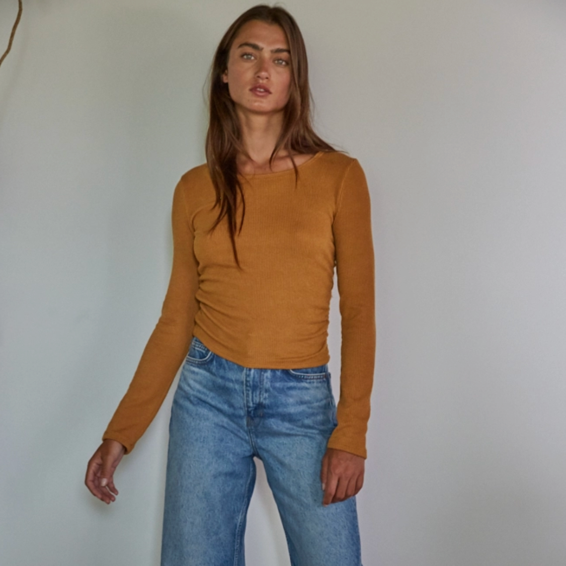 Woman wearing a Carmel long-sleeve top and blue jeans against a plain background