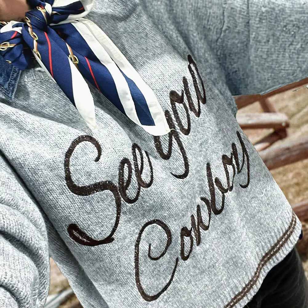 Gray sweater with 'See you cowboy' text and a scarf, worn by a person.