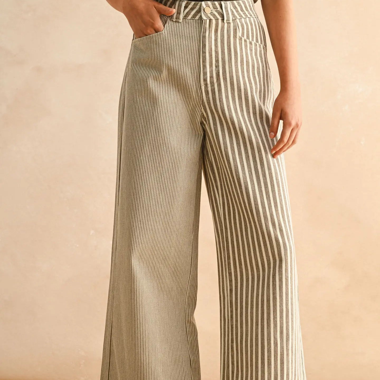 Person wearing a brown top and beige and white striped wide-leg pants against a beige background