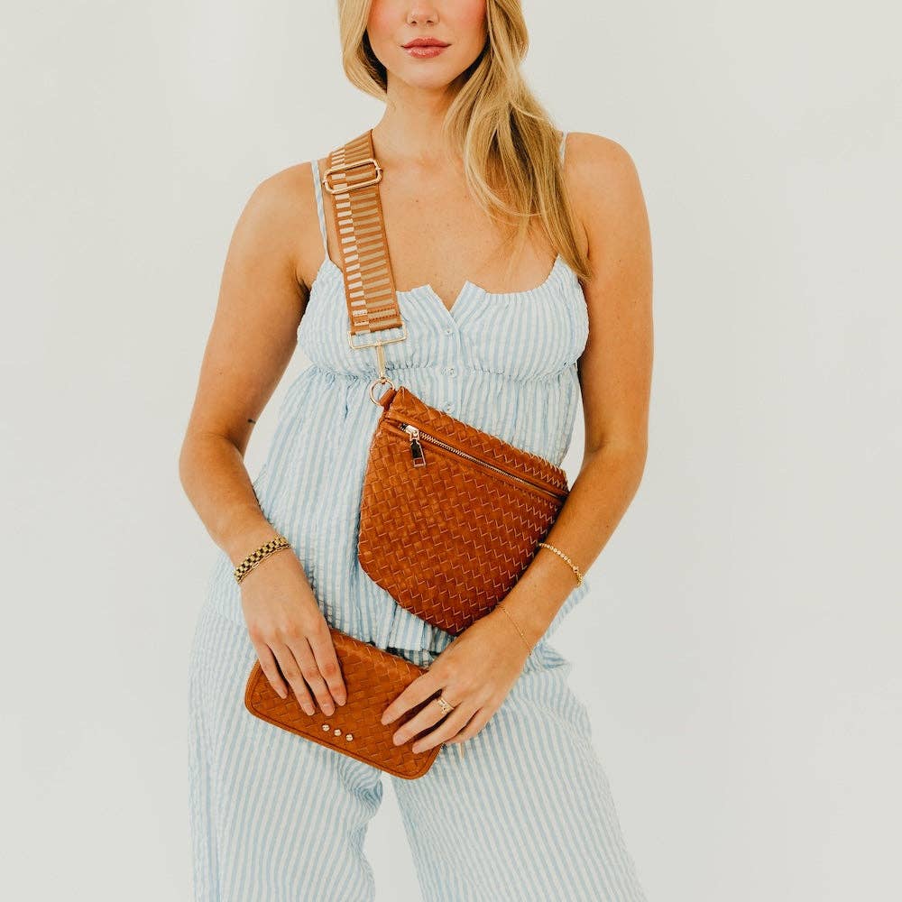 Woman holding a brown woven bum bag handbag against a plain background