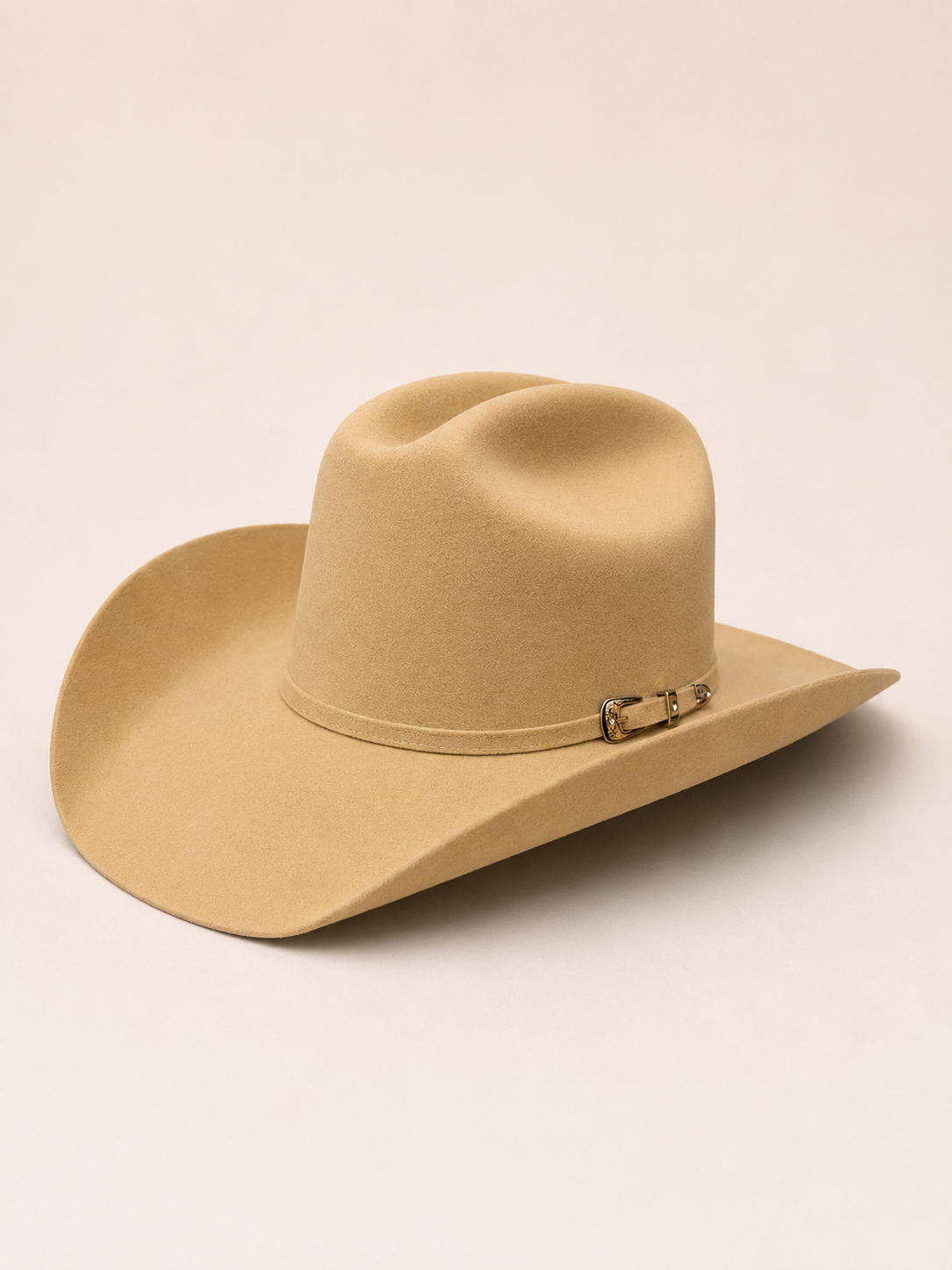A light tan wool felt cowboy hat with a curved brim and a small gold-tone metal buckle detail on the band, shown against a solid light beige background.