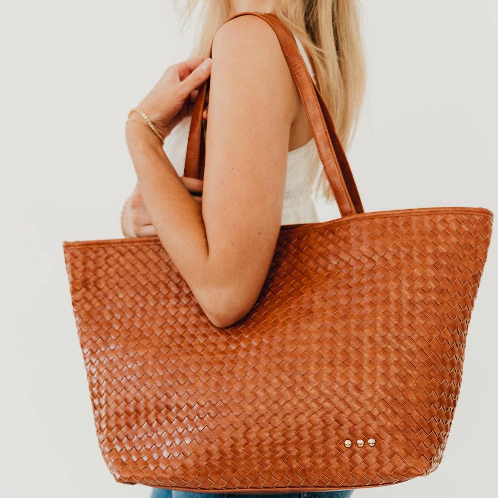 Woman wearing a cozy cream off shoulder sweater while carrying a beige studded crossbody bum bag against a neutral background